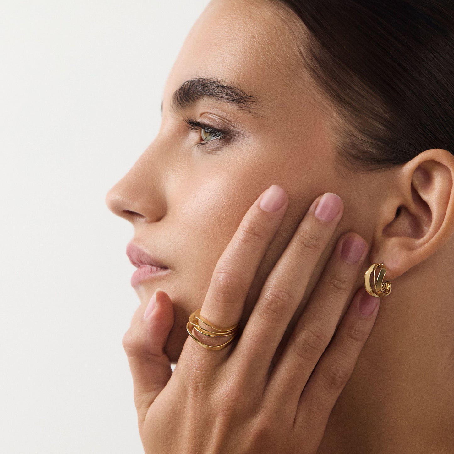 Woman wearing gold earrings and rings on a plain background