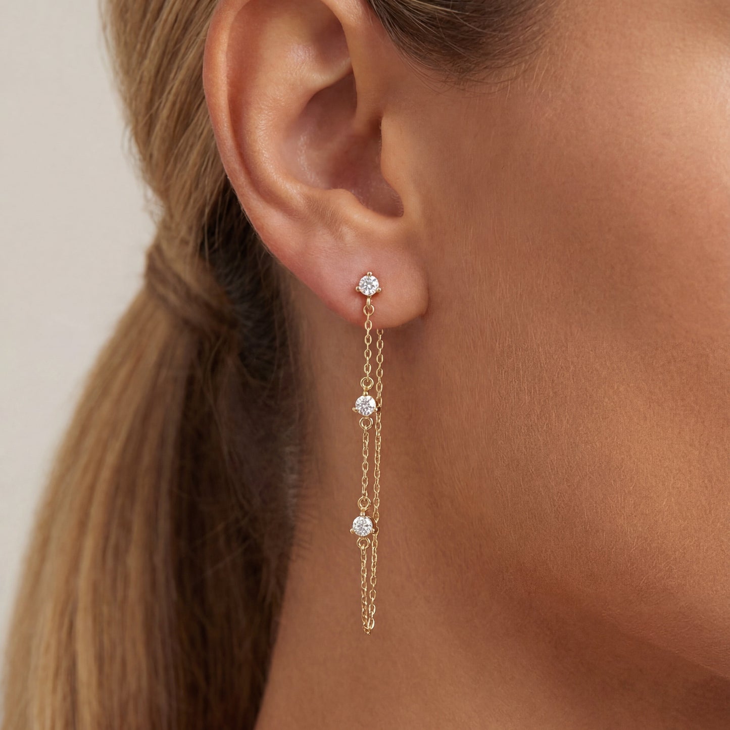 Gold earrings with small stones worn by a person with a ponytail.