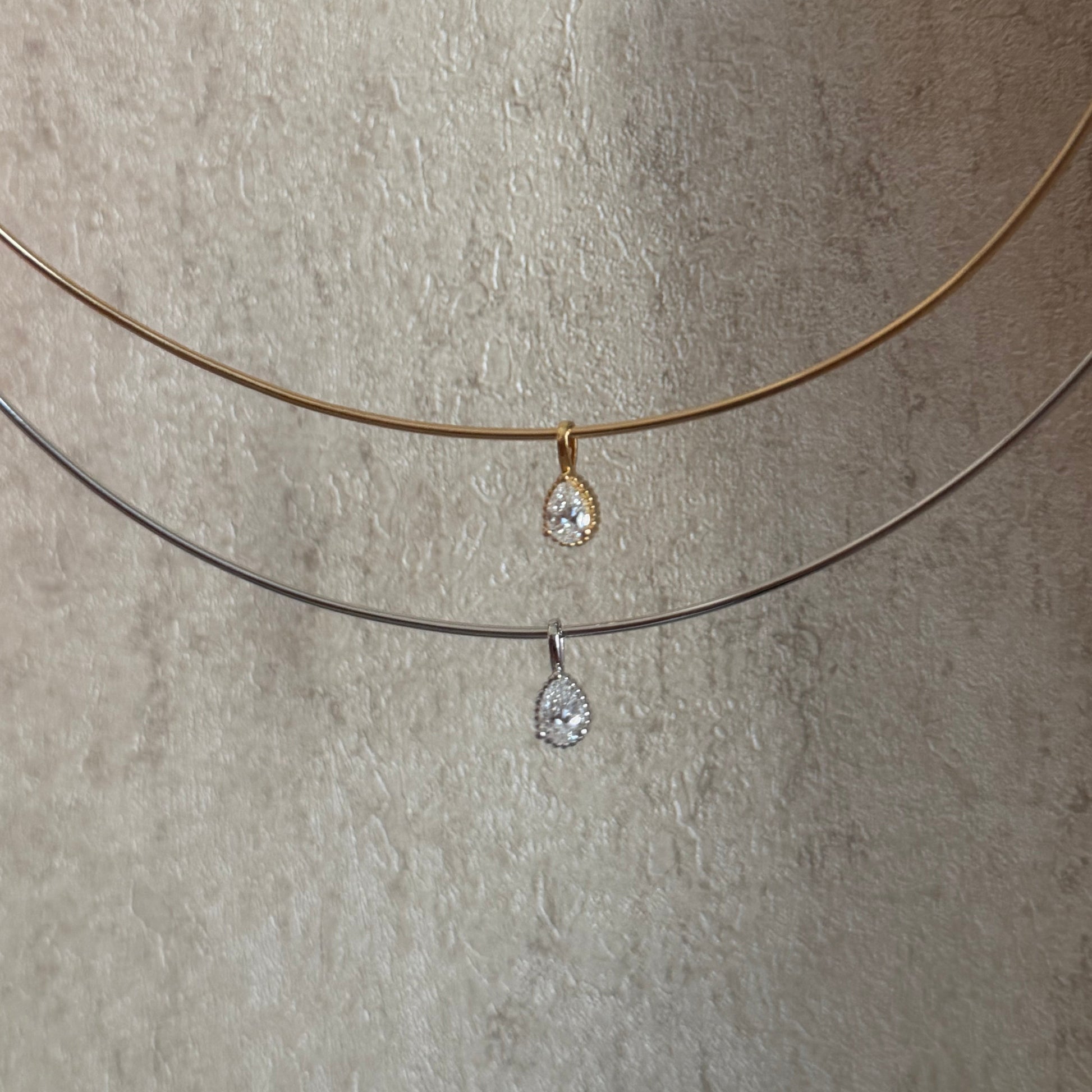 Two necklaces with teardrop-shaped pendants on a textured beige surface.