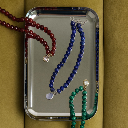 Three beaded necklaces in red, blue, and green on a mirror with a gold background