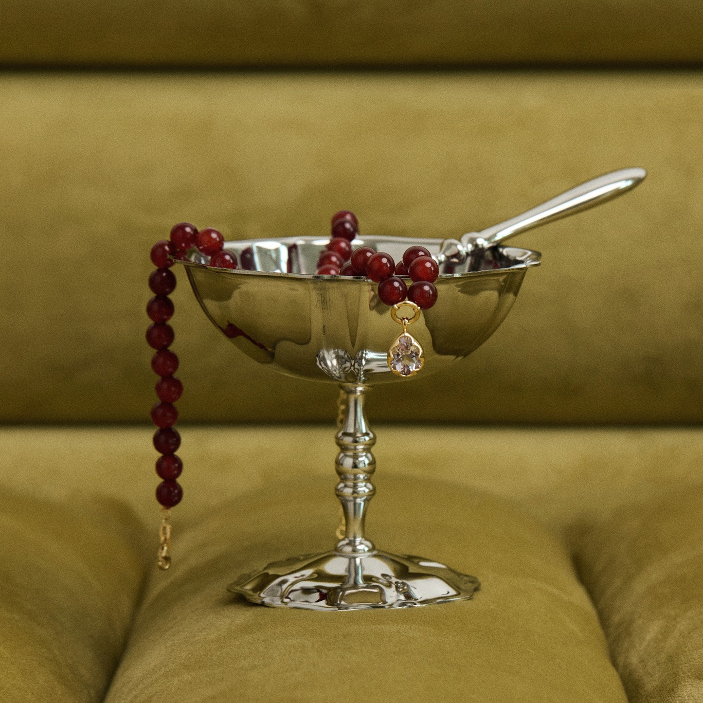 Silver bowl with berries and a spoon on a green cushion