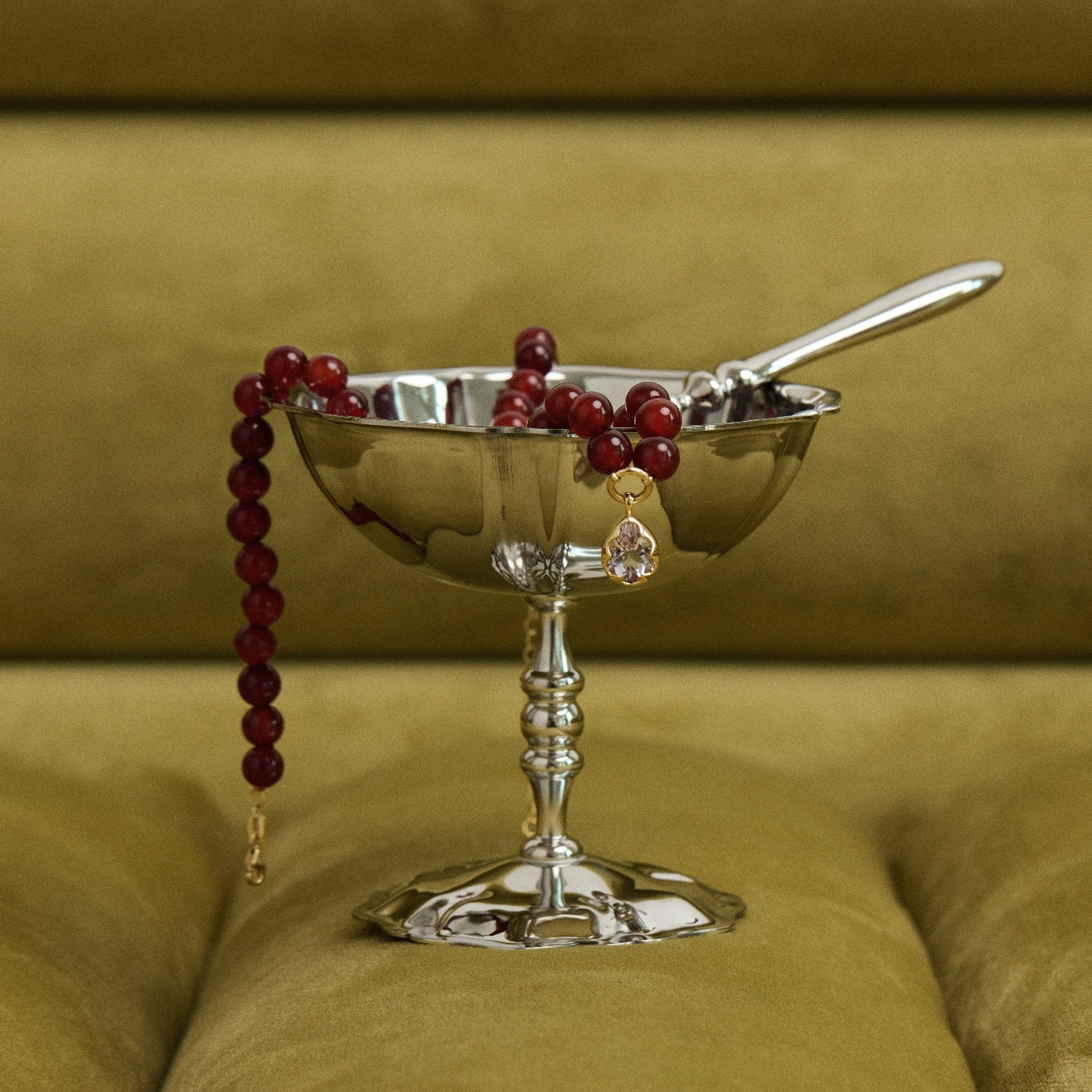 Silver bowl with berries and a spoon on a green cushion