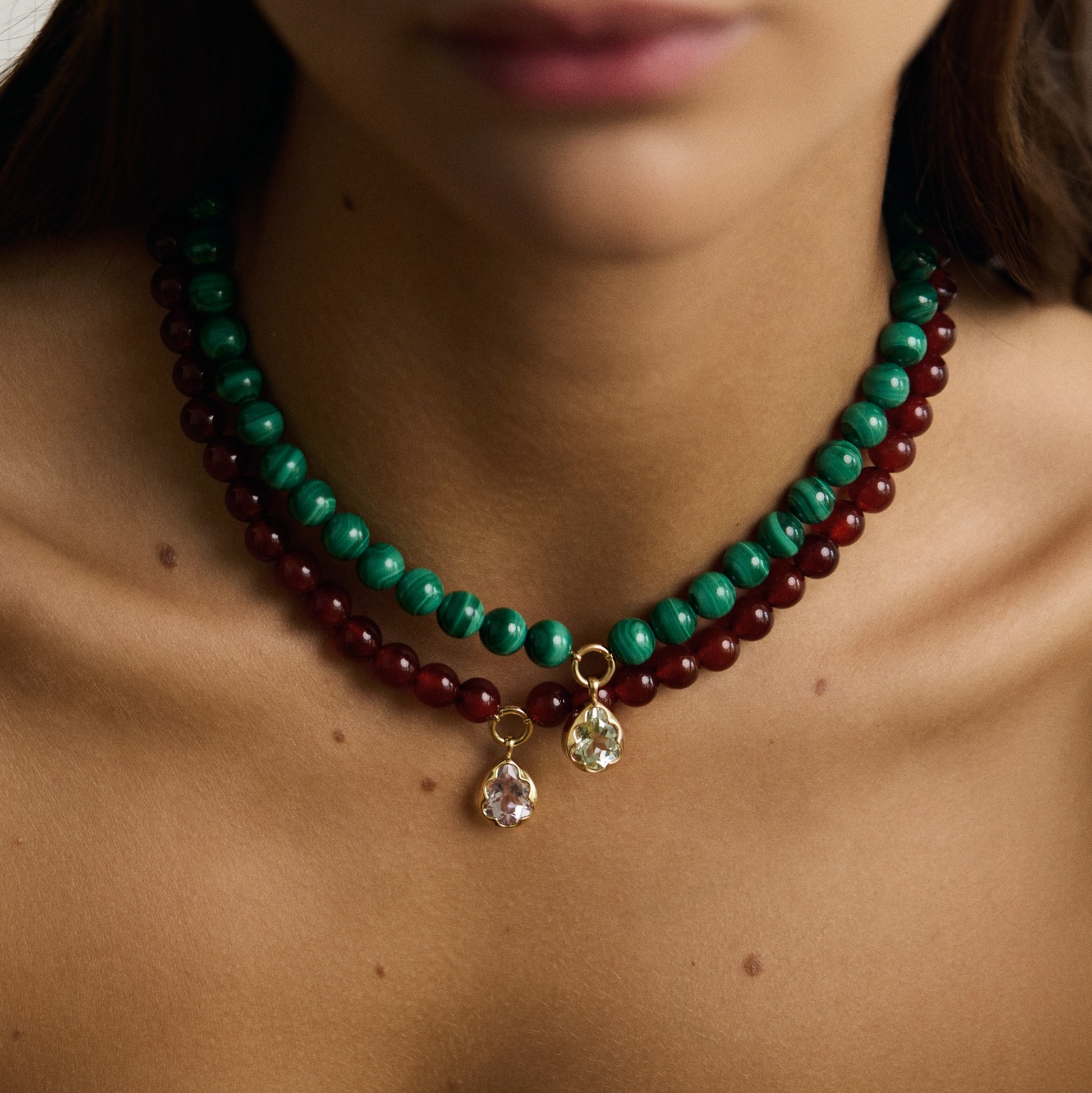 Close-up of a person wearing a green and red beaded necklace with a pendant.