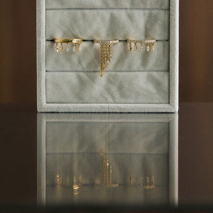 Gray jewelry box with gold jewelry on a reflective surface and brown background