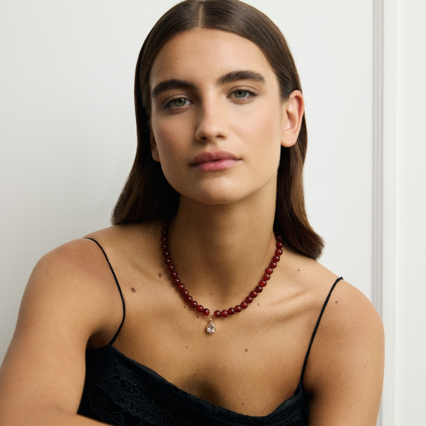 Woman wearing a black dress and red necklace against a white background