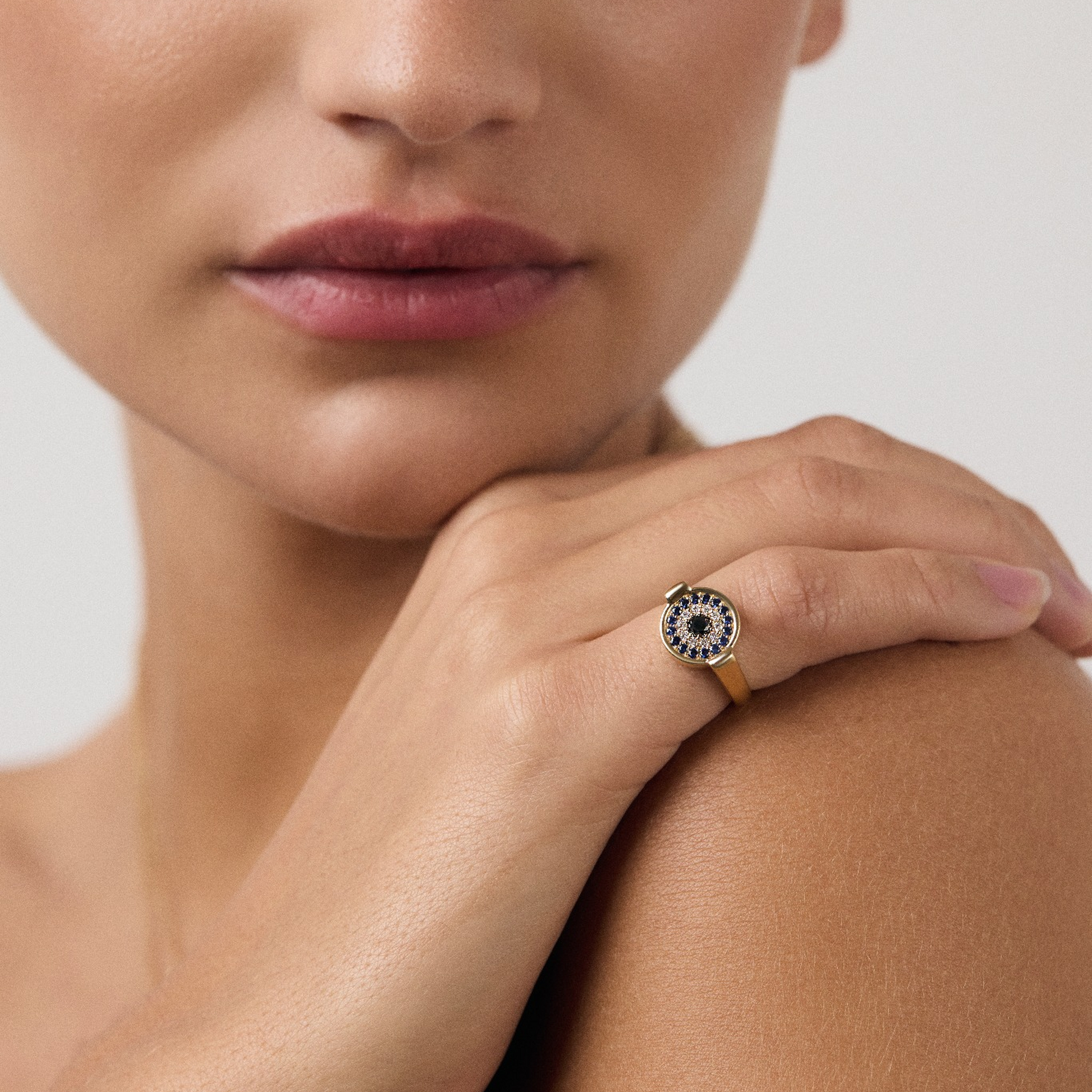 Close-up of a woman's face with a ring on her finger, wearing a black and gold ring.