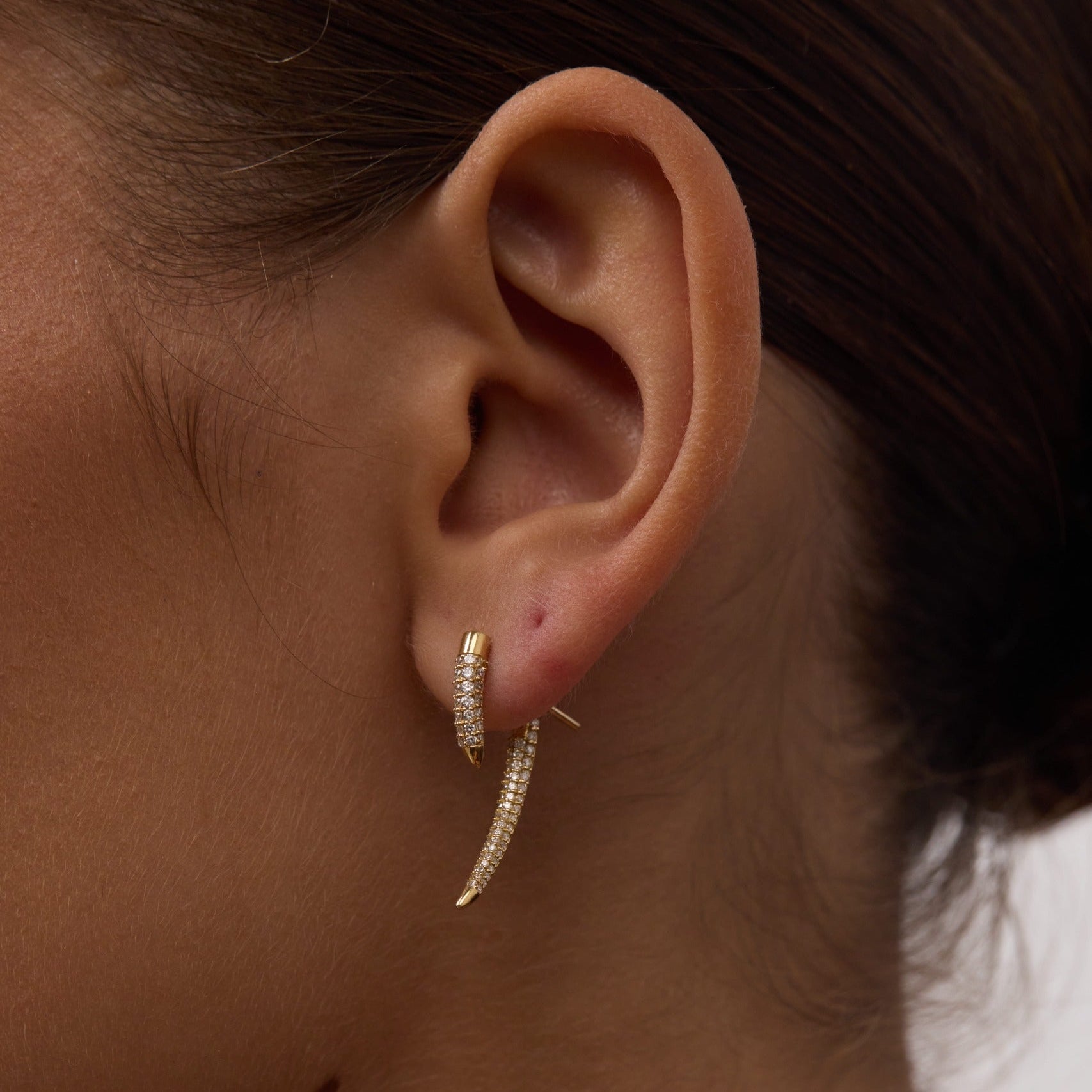 Close-up of an ear wearing a gold hoop earring with a blurred background