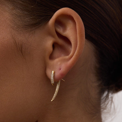 Close-up of an ear wearing a gold hoop earring with a blurred background