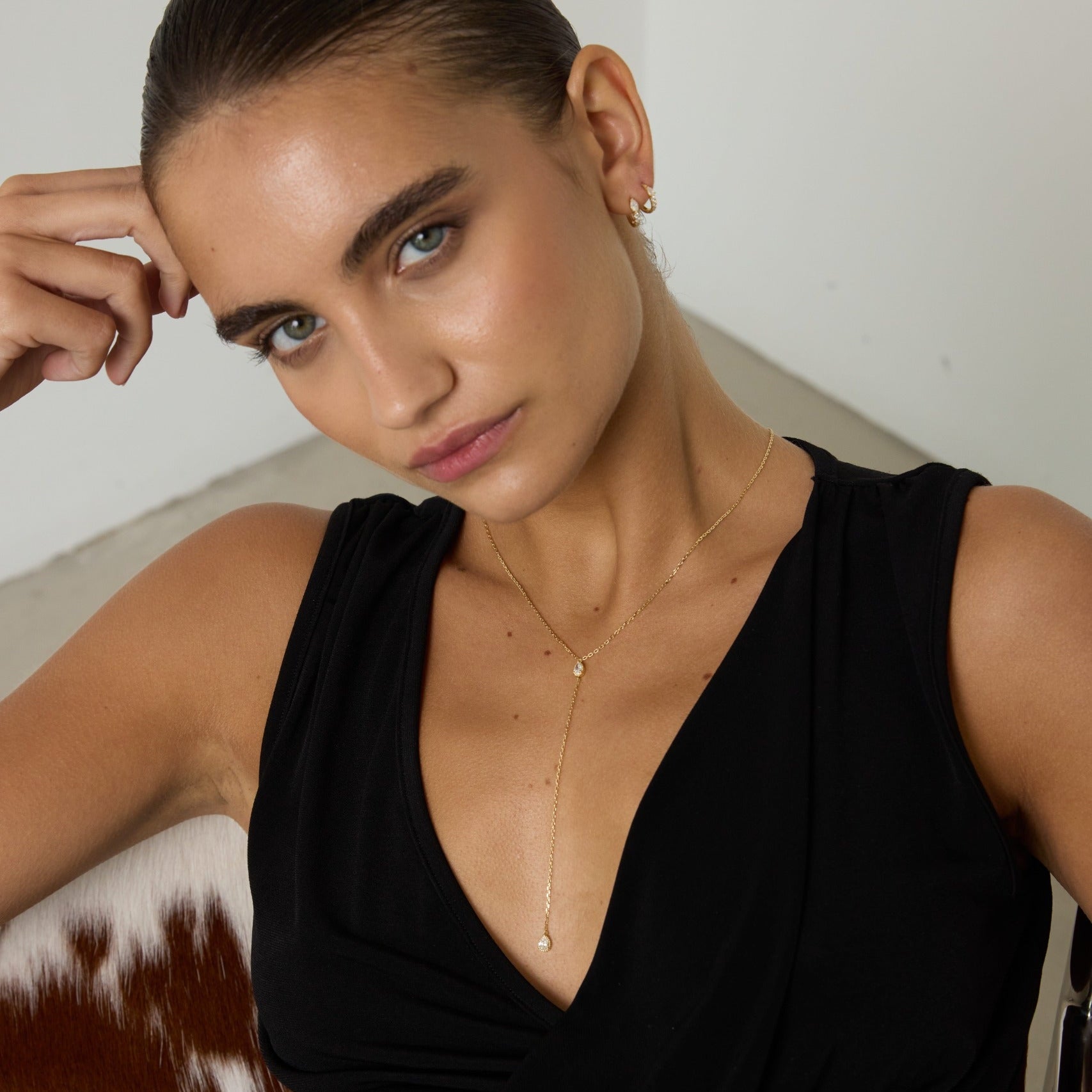 Woman wearing a black sleeveless top with a gold necklace against a neutral background