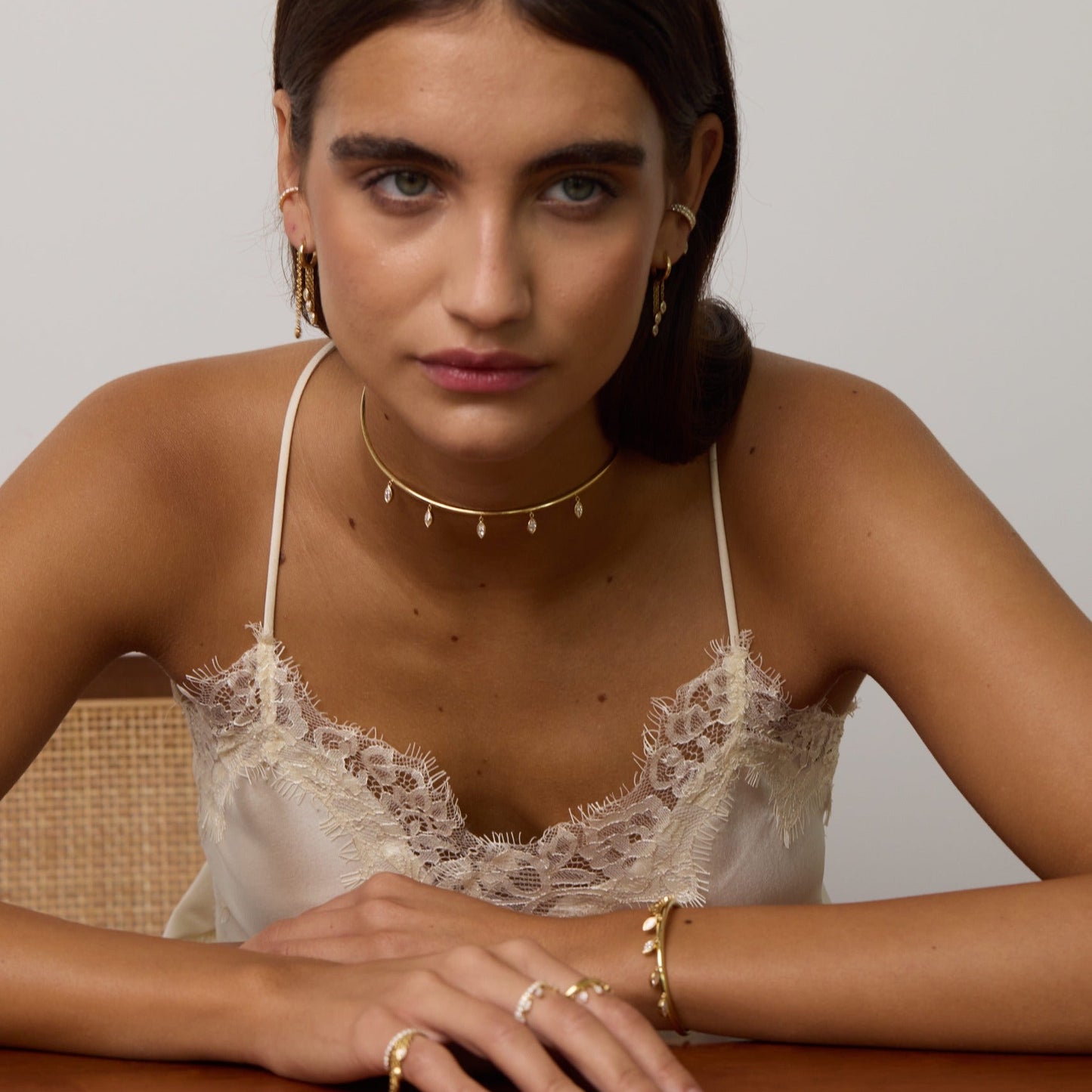 Woman wearing a lace top and gold jewelry on a wooden table with a neutral background