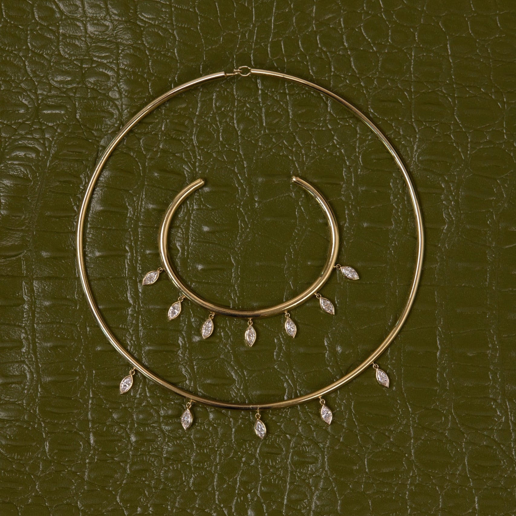 Gold hoop earrings with small dangling stones on a textured green surface