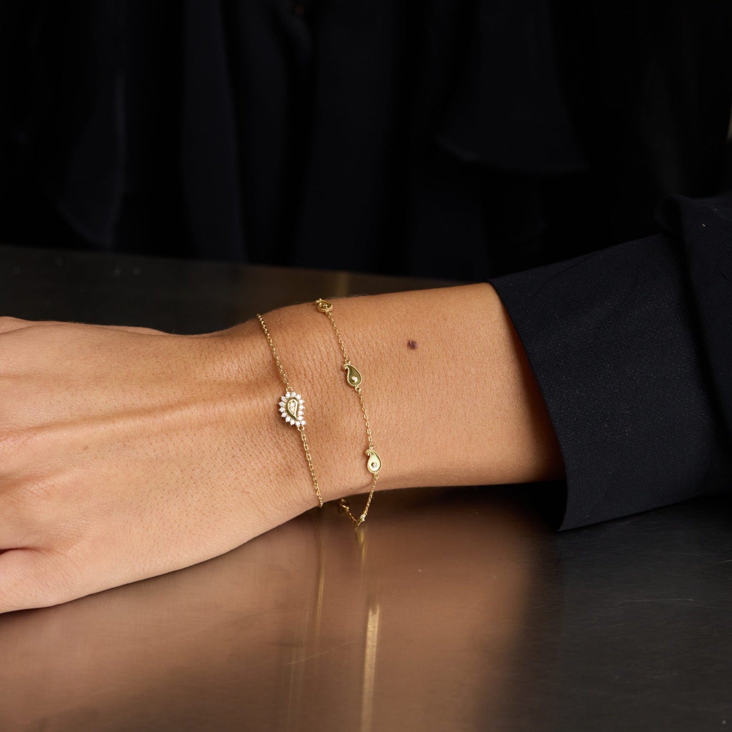 Close-up of a person's wrist wearing multiple gold bracelets on a dark surface