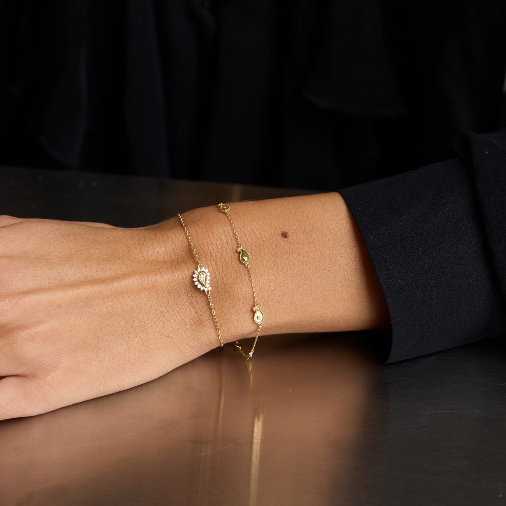 Close-up of a person's wrist wearing multiple gold bracelets on a dark surface