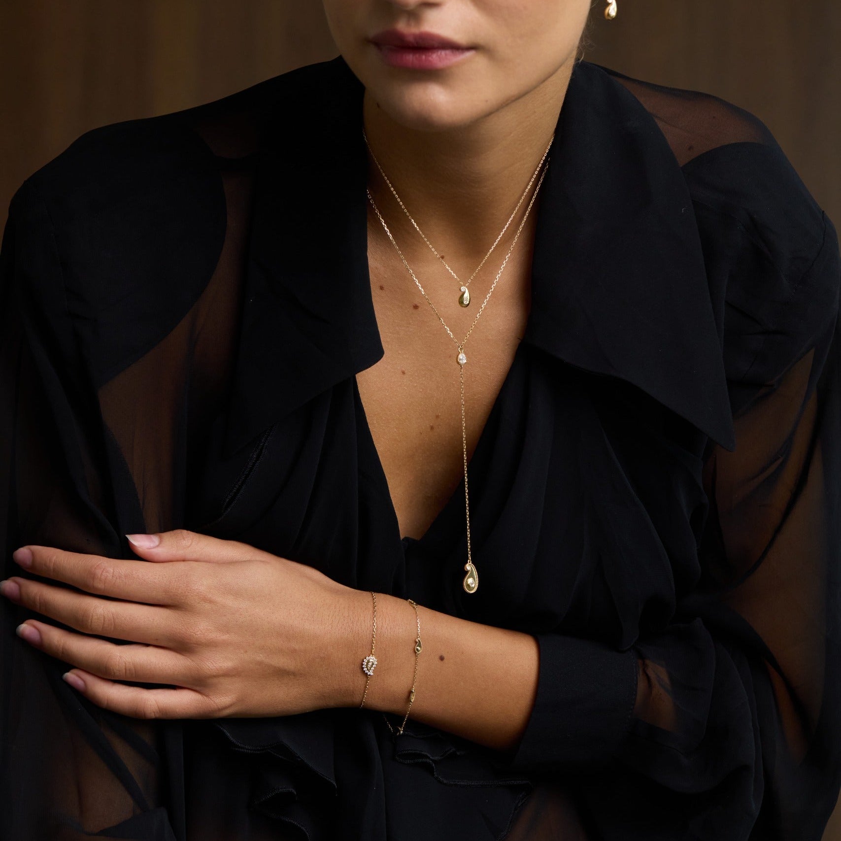 Woman wearing a black sheer top with visible jewelry against a brown background