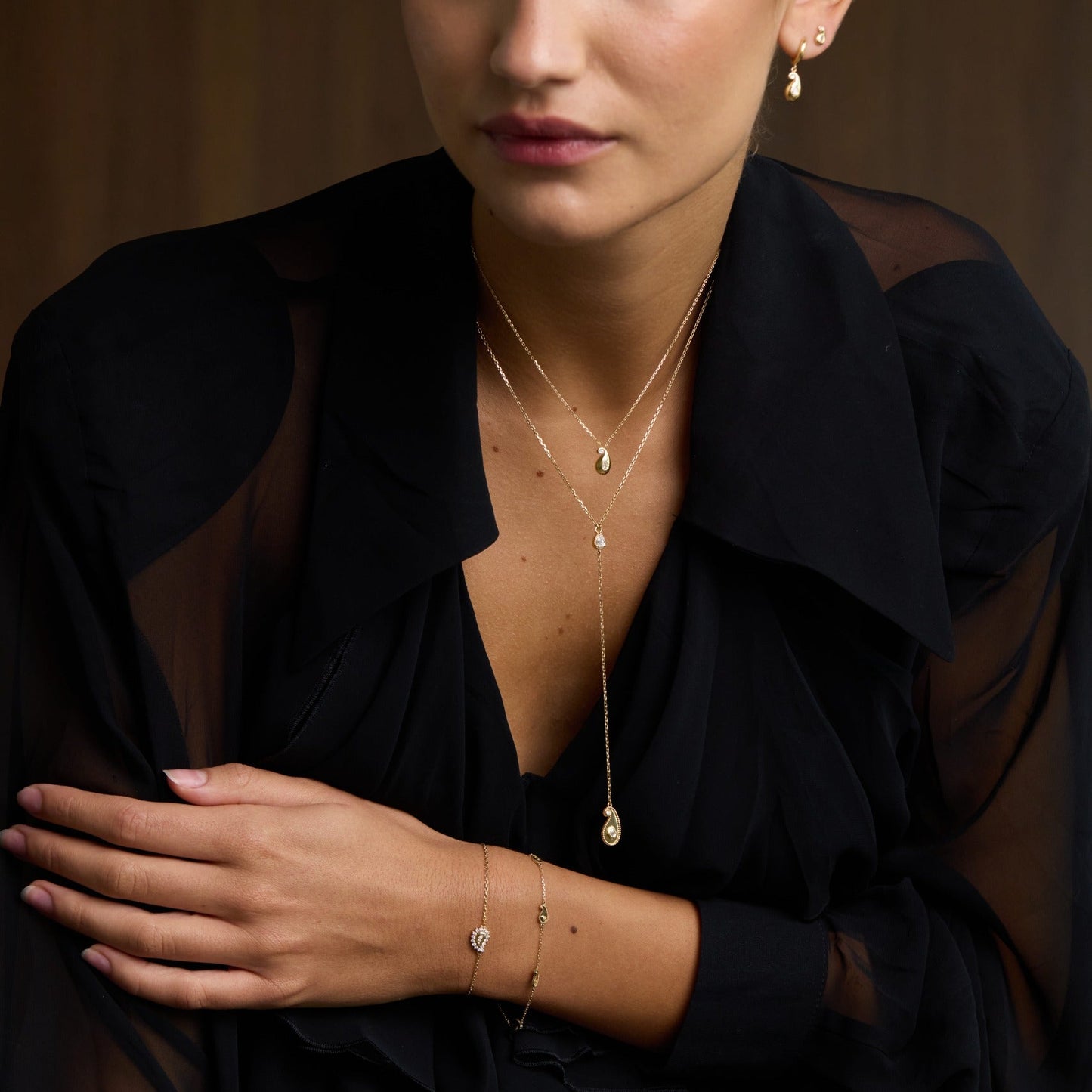 Woman wearing a black sheer top with visible jewelry against a brown background