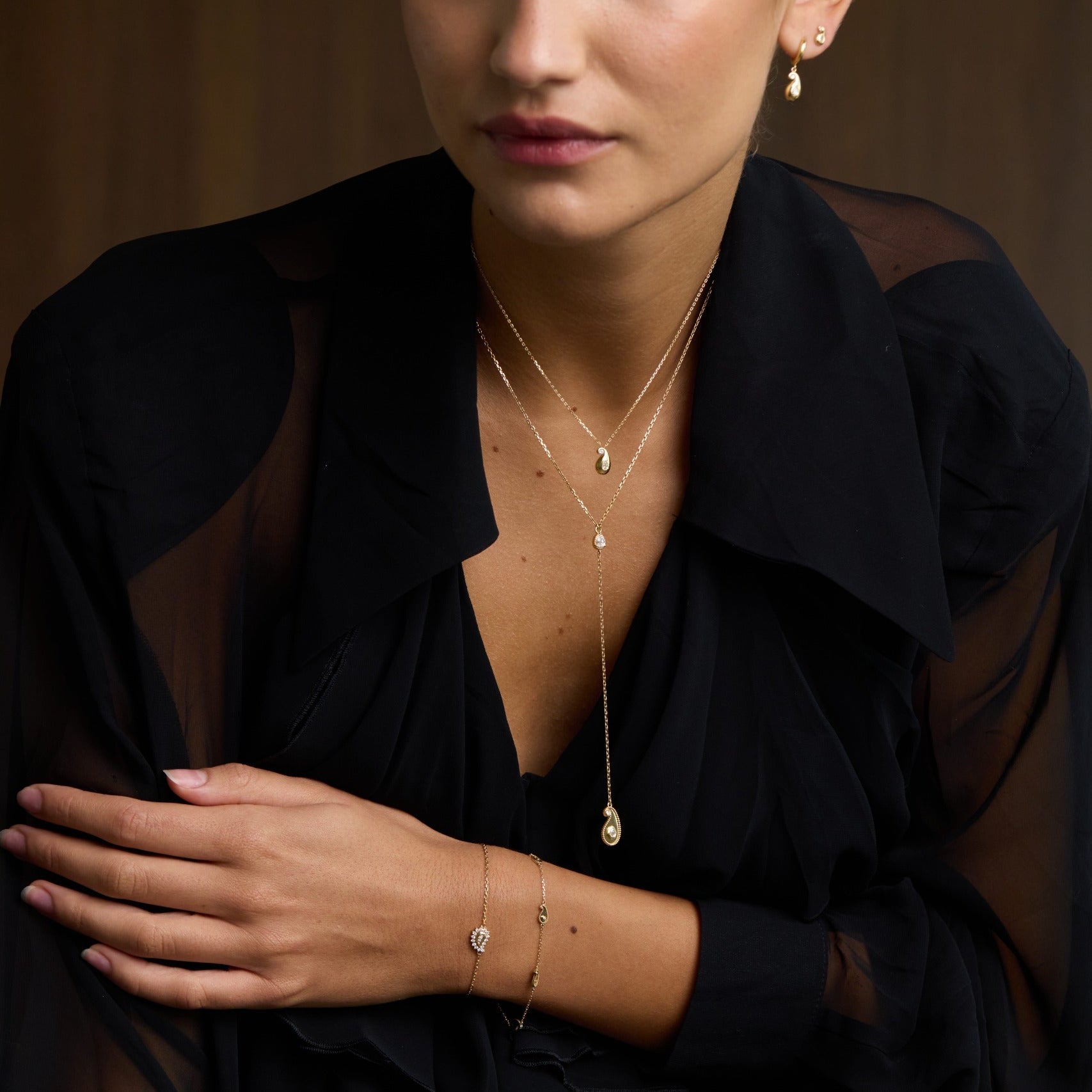 Woman wearing a black sheer top with visible jewelry against a brown background