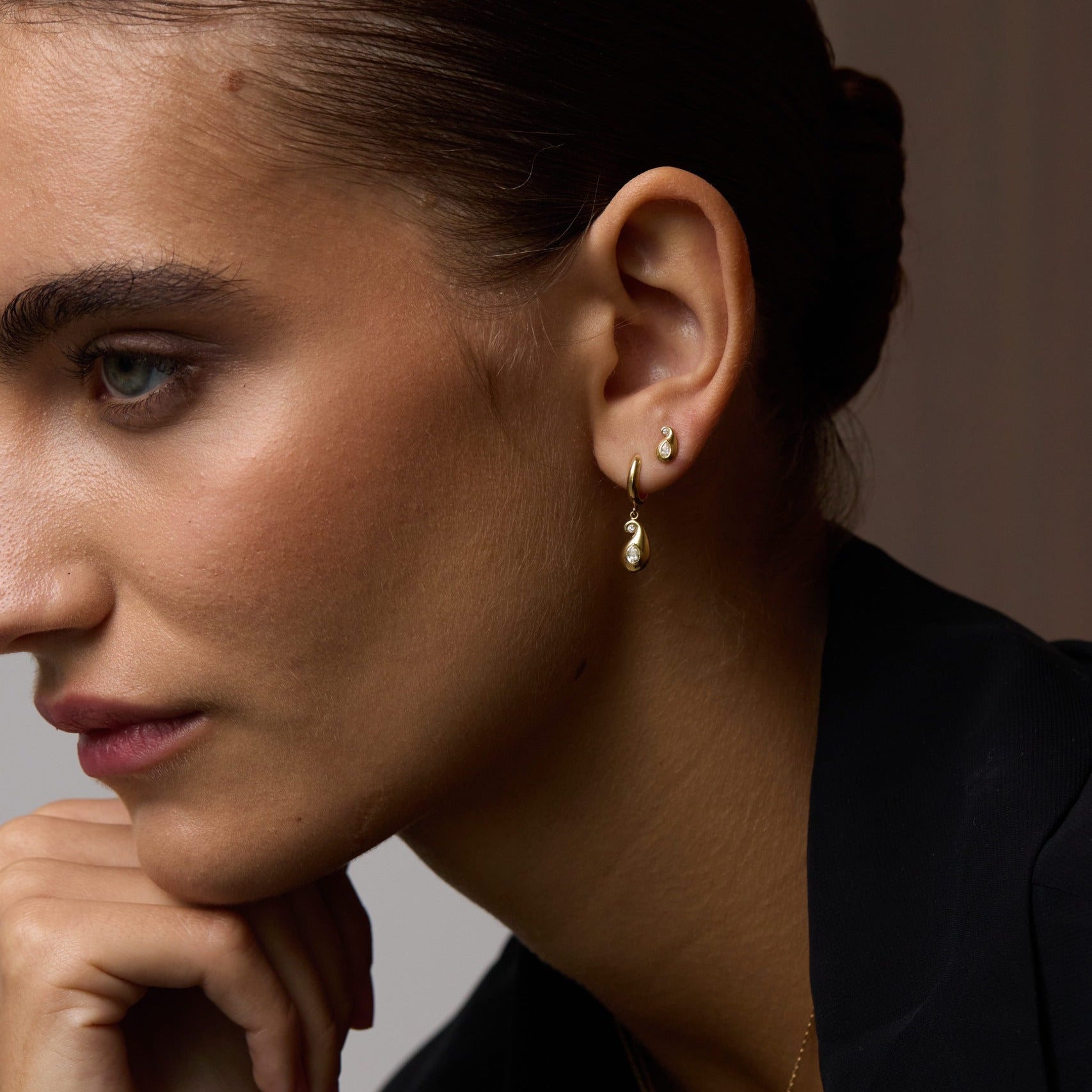 Close-up of a woman wearing gold earrings and a necklace against a neutral background