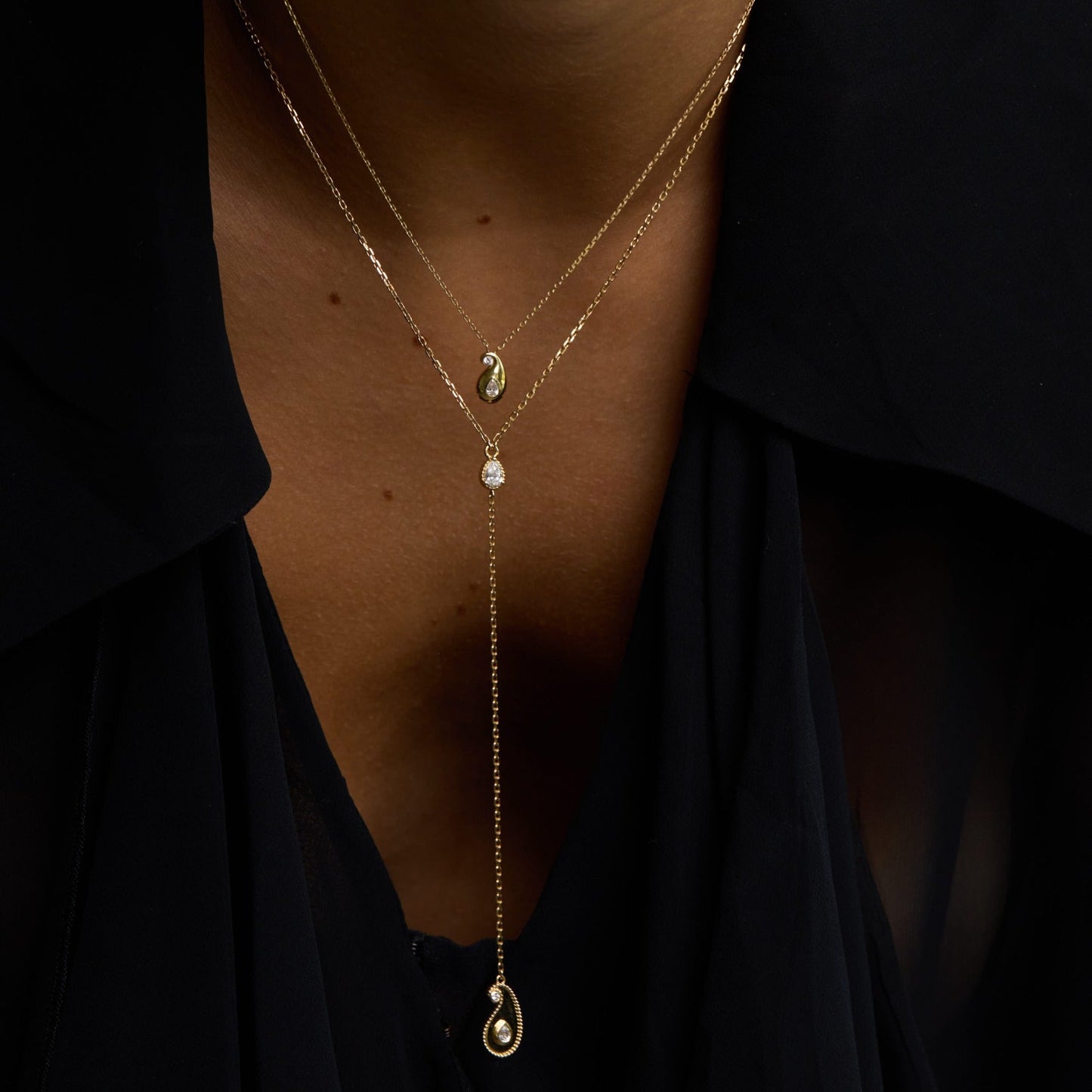 Close-up of a person wearing a delicate gold necklace with small pendants against a dark background.