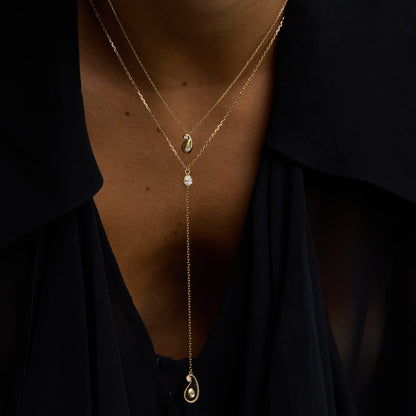 Close-up of a person wearing a delicate gold necklace with small pendants against a dark background.