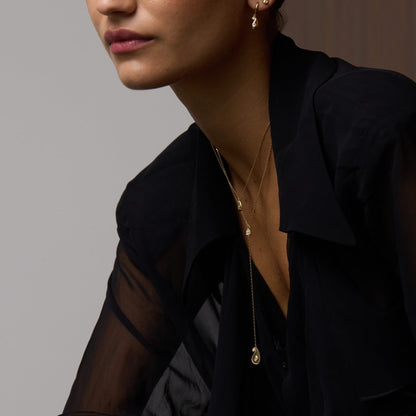 Woman wearing a black outfit with sheer sleeves and gold jewelry against a neutral background