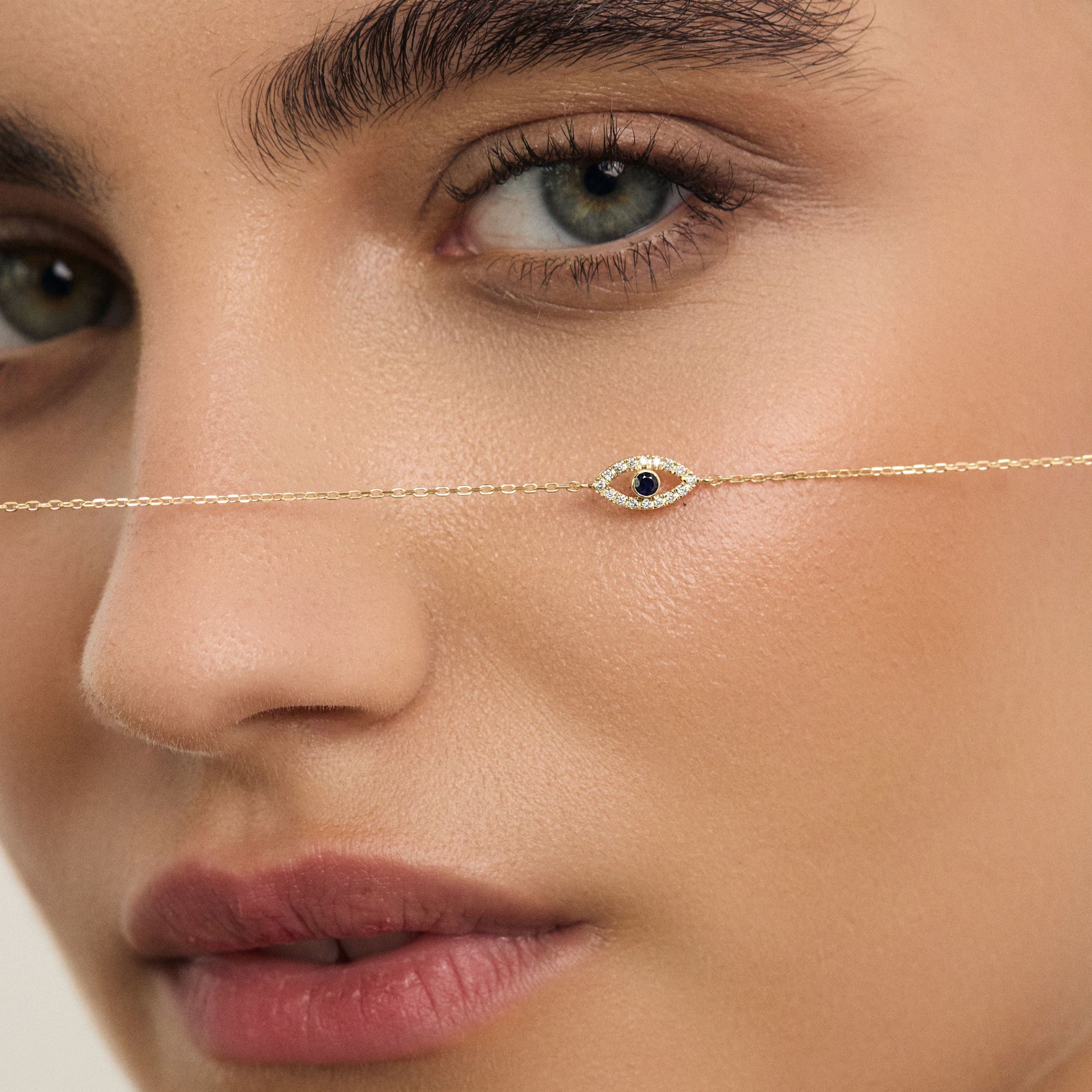 Close-up of a woman's face wearing a delicate gold necklace with a blue gemstone.