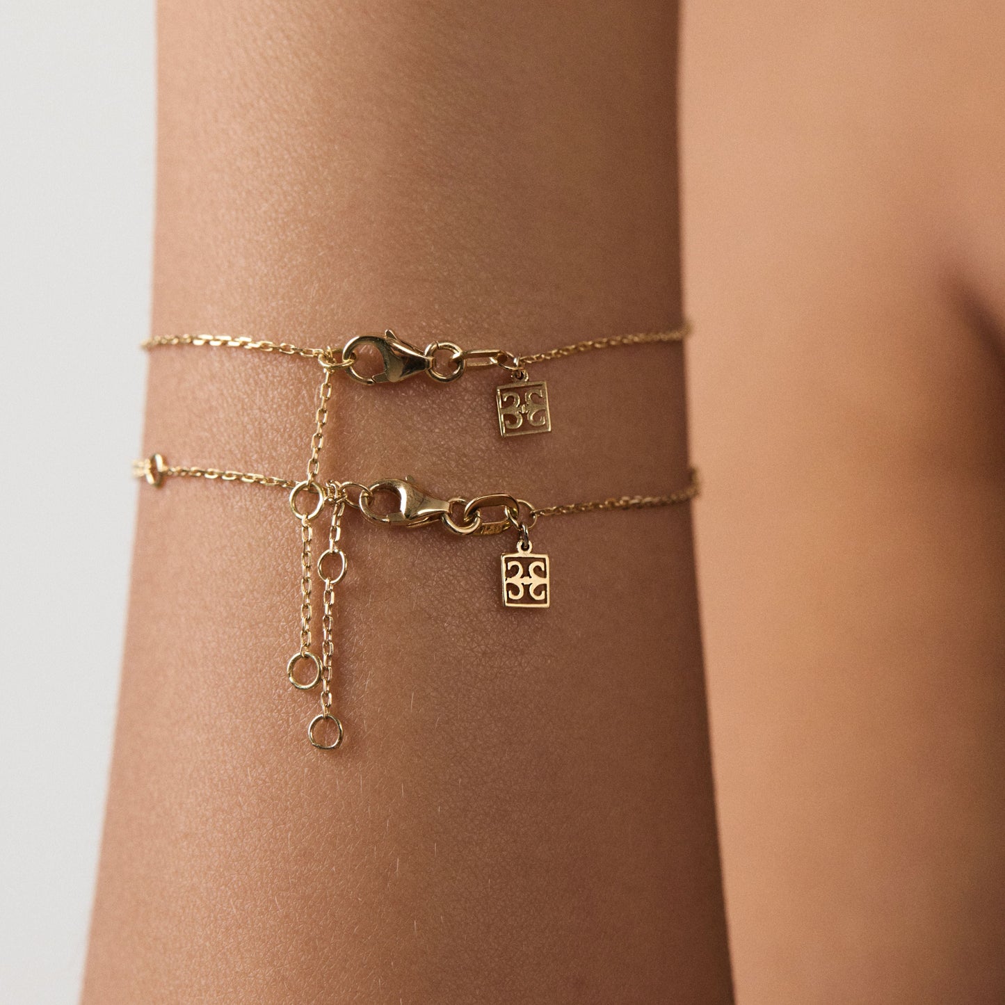 Gold bracelet with charms on a wrist against a neutral background