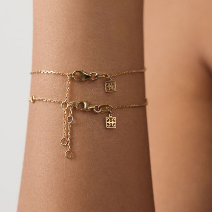 Gold bracelet with charms on a wrist against a neutral background