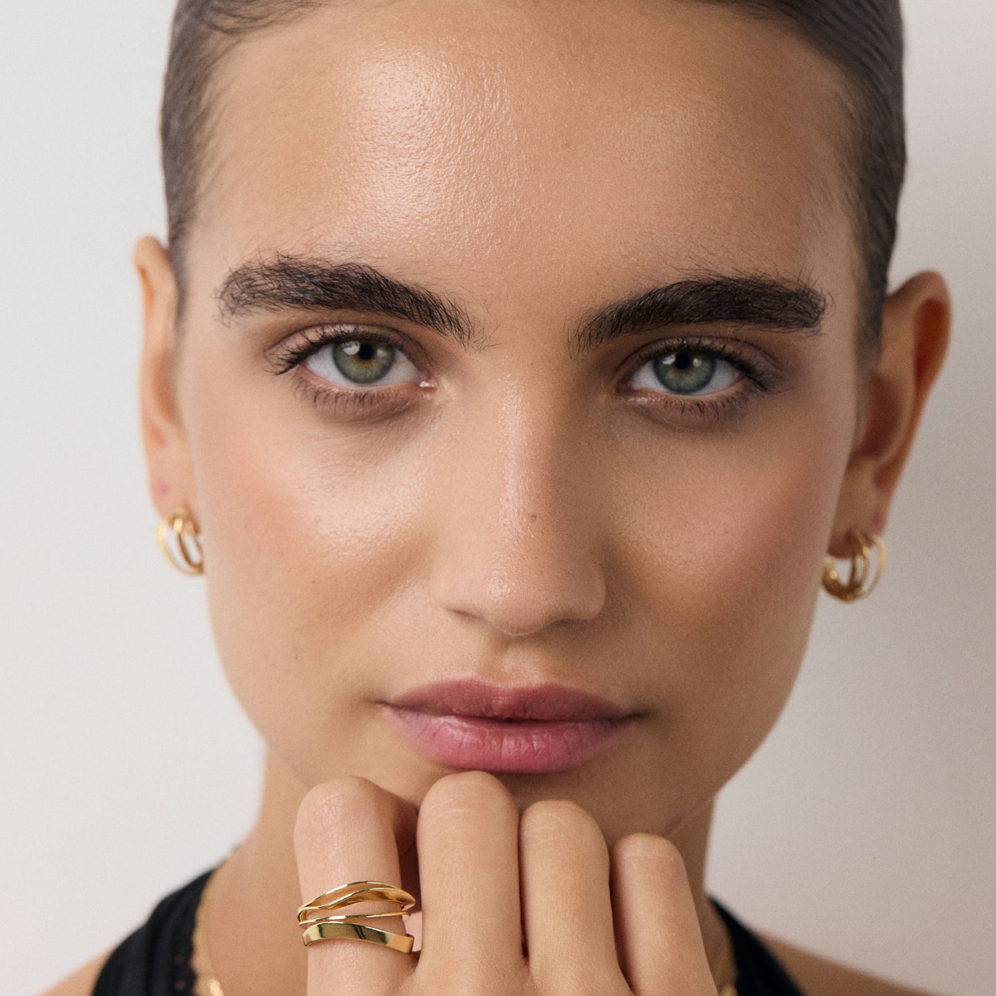 Close-up of a woman wearing gold jewelry against a neutral background