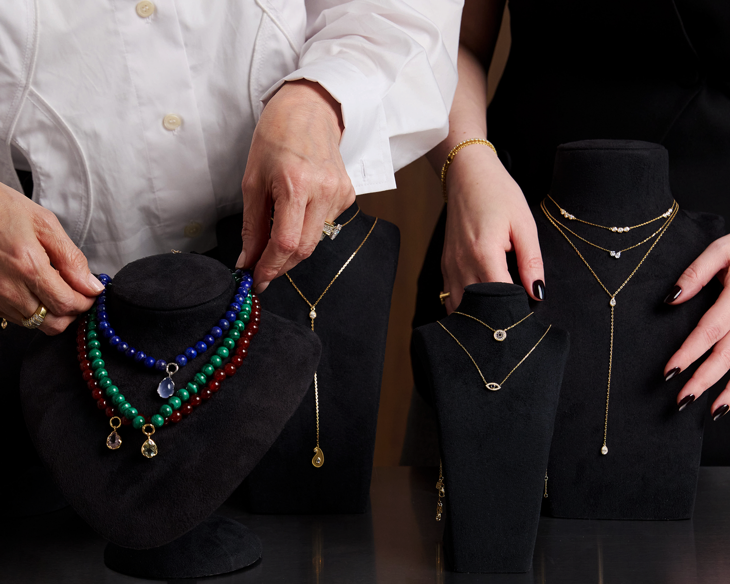 Person arranging necklaces on black stands with a focus on jewelry display.