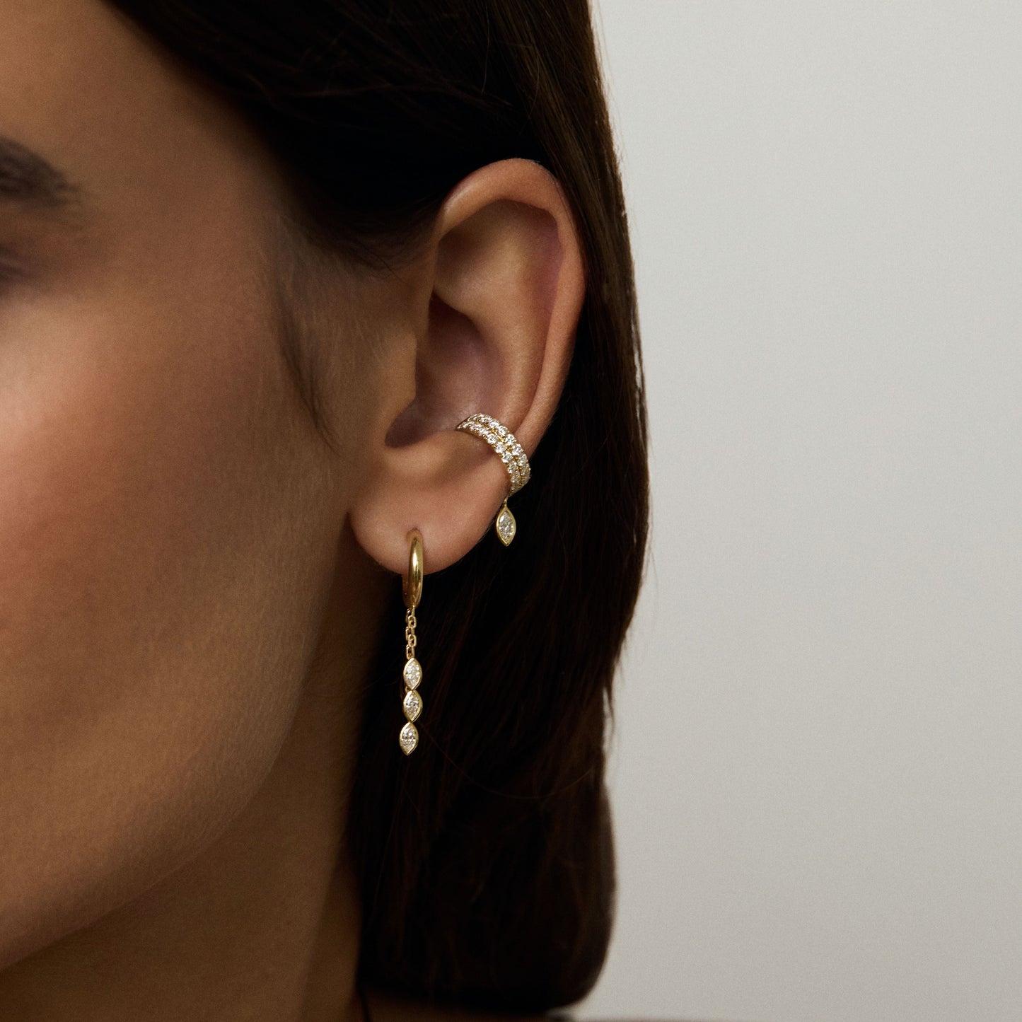 Close-up of a person wearing gold hoop earrings with dangling beads on a neutral background
