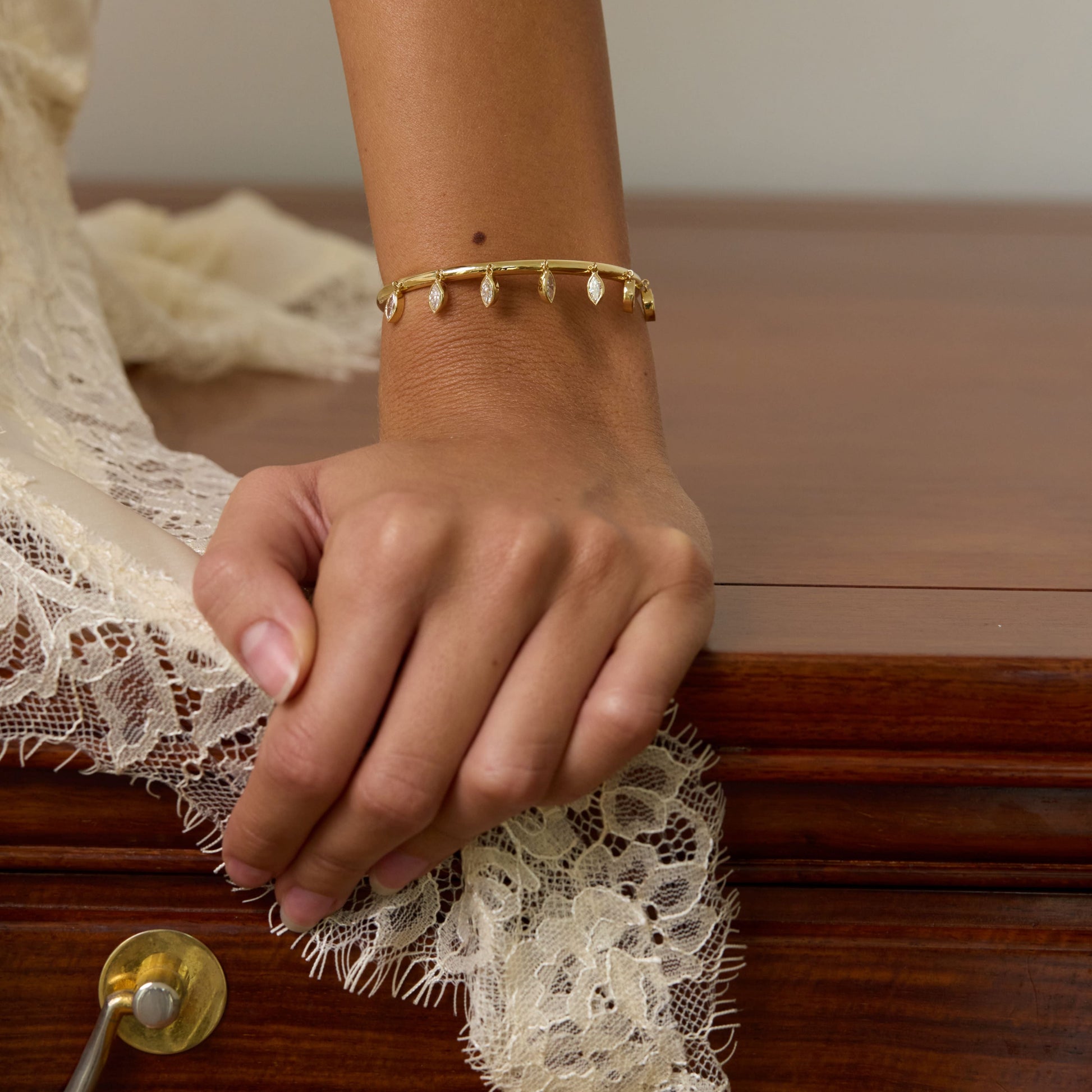 Hand with a gold bracelet on a wooden surface with lace fabric