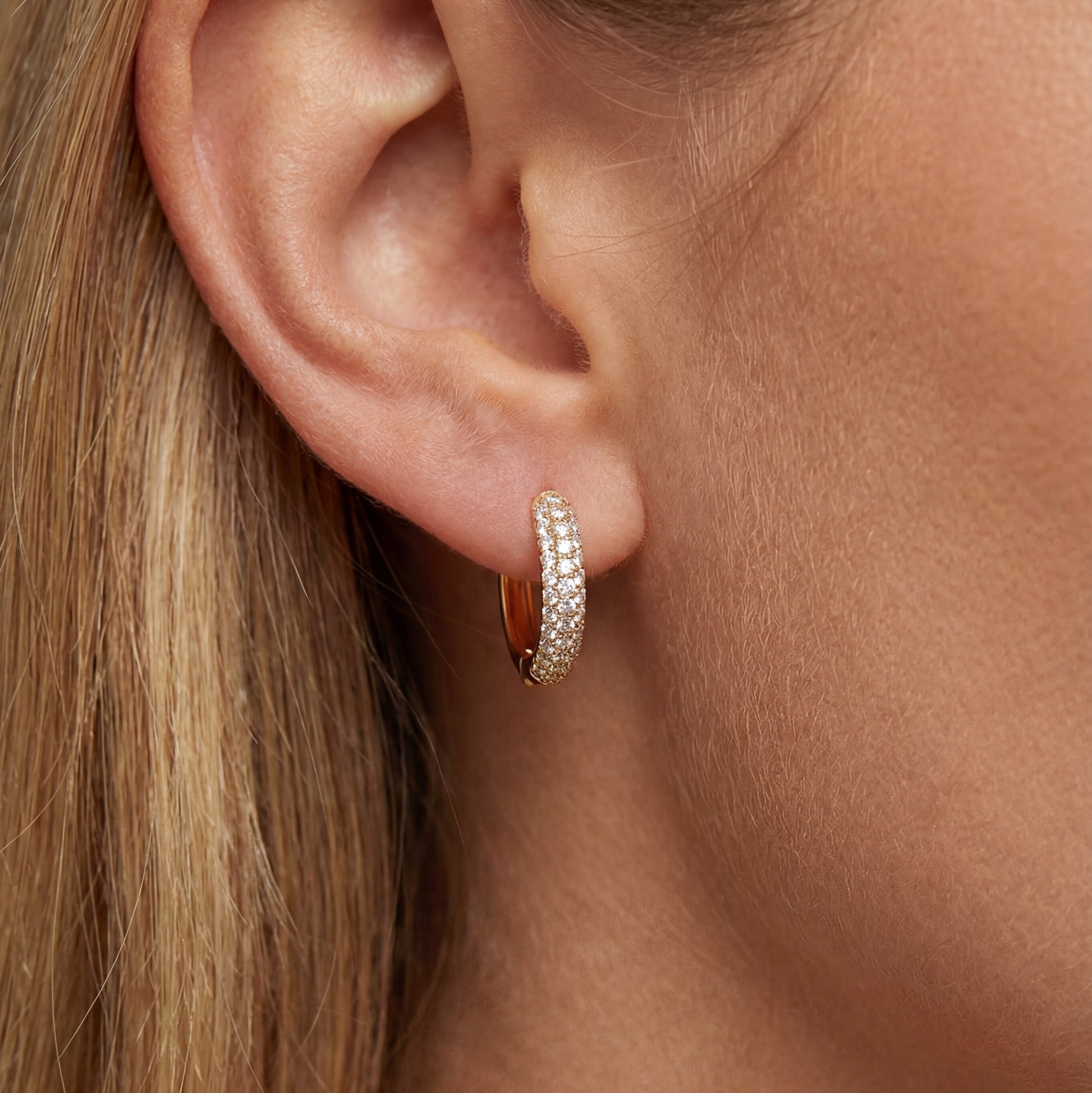 Close-up of an ear wearing a gold hoop earring with clear stones.