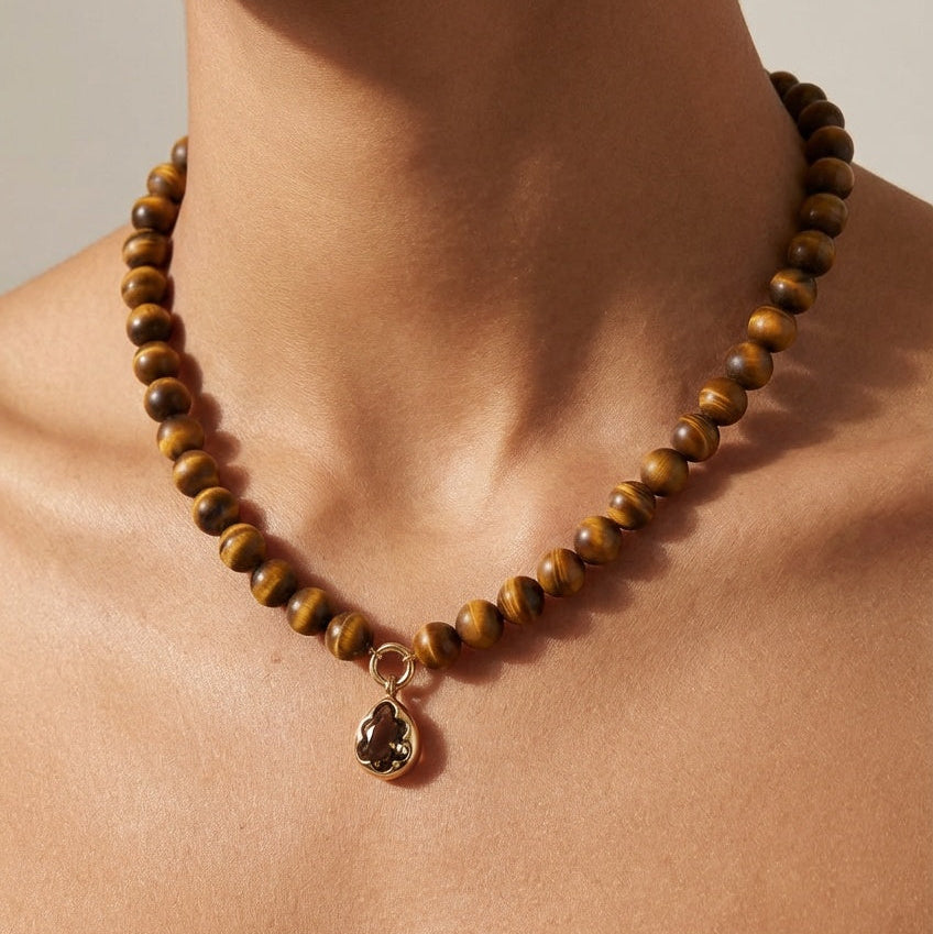 Necklace with brown beads and a pendant on a person's neck against a neutral background