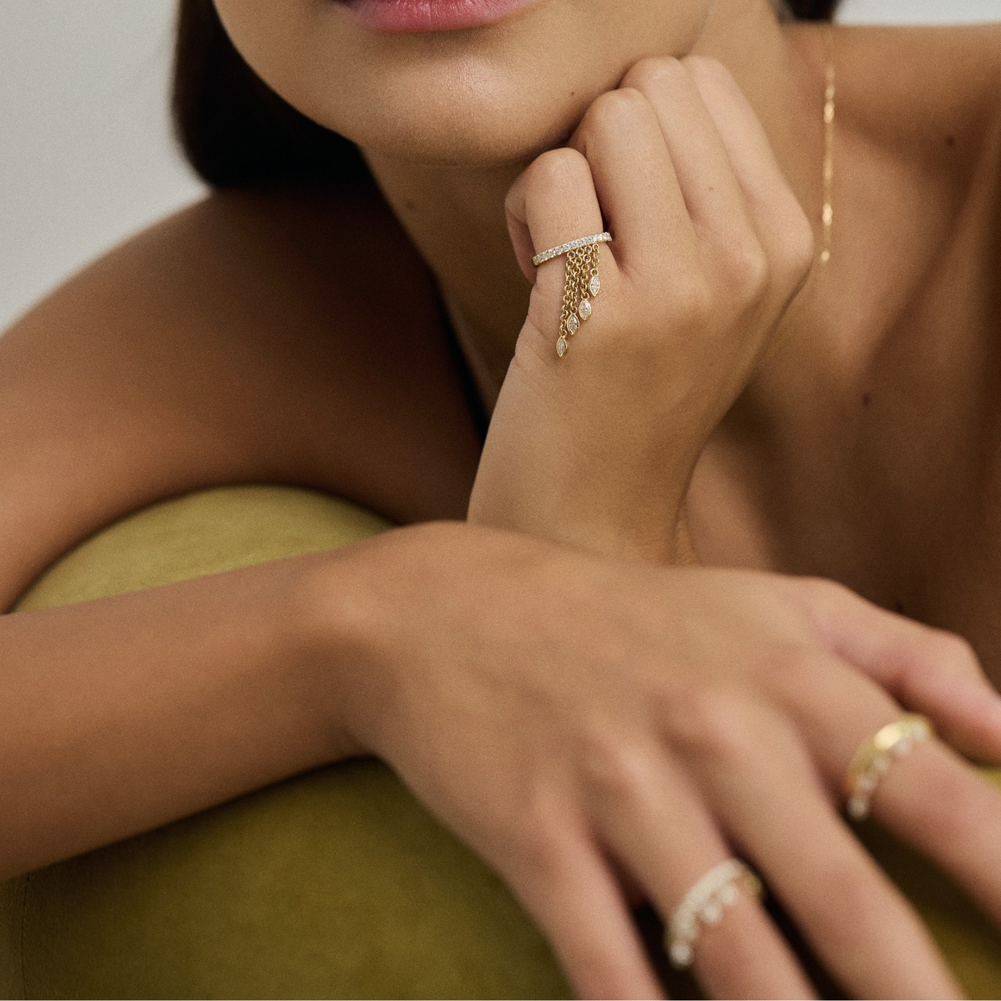 Woman wearing gold jewelry including earrings, necklace, and rings on a neutral background